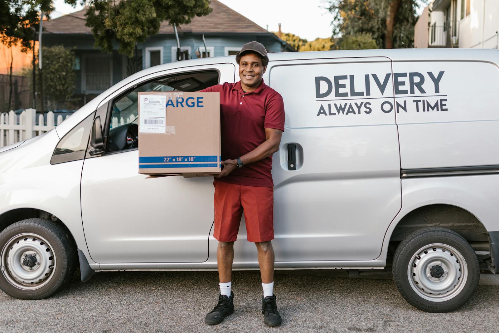 A courier in a maroon uniform smiling with a package in front of a delivery van, commercial auto